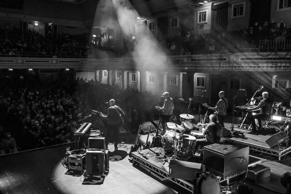 A black and white photo taken from behind Lindisfarne as they play on stage in front of a large crowd