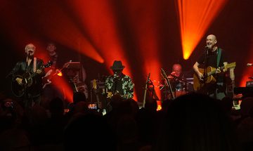 Lindisfarne on stage performing with orange lights behind them