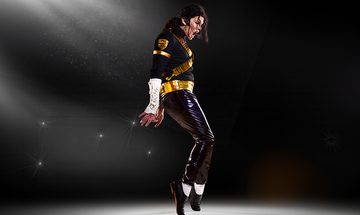 A Michael Jackson impersonator in a shiny black costume with golden details stood on his toes mid dance with a spotlight on him on a black background