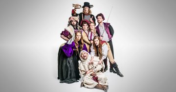 Eight people, four men and four women, in Tudor clothing, all stood looking very serious other than one man on the floor who is laughing with a mobile phone and empty liquor bottle in hand