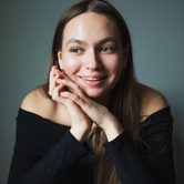 a headshot of Rose McLachlan - she wears all black and rests her hands on her face. She smiles off to the side
