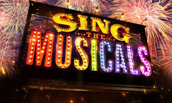Sing the Musicals is written on a large sign. Each letter is a different colour of the rainbow and is lit with light bulbs like a Hollywood-style mirror. Behind the sign fireworks can be seen in the sky