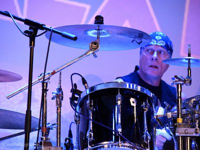 A man in a bandana, plays the drums while looking to the side of him