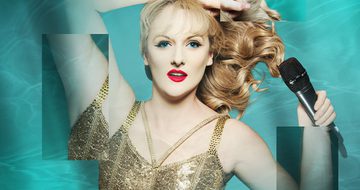 A Taylor Swift impersonator laying on a water background in a gold strappy top holding a microphone