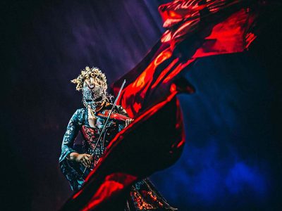 a woman playing the violin wearing a mask and a long flowing red cape