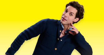 Tom Wilson, a young white man with curly black hair in a dark blue shirt. he is resting his head on the fingers of his right hand. He is looking surprised at the camera