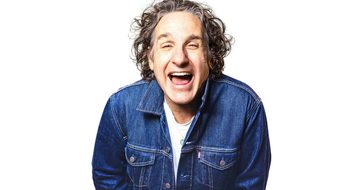 Tom Stade laughing with his mouth open in a denim jacket on a white background