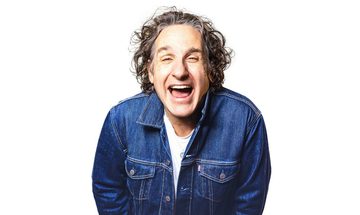 Tom Stade laughing with his mouth open in a denim jacket on a white background