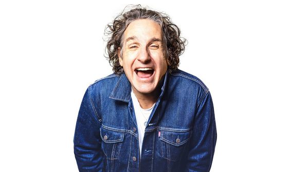 Tom Stade laughing with his mouth open in a denim jacket on a white background
