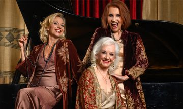 Comedy singing group Fascinating Aïda smiling in matching nightwear next to a piano, with two sitting and one standing