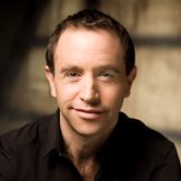 Mark Wigglesworth wearing a black shirt, smiling at the camera