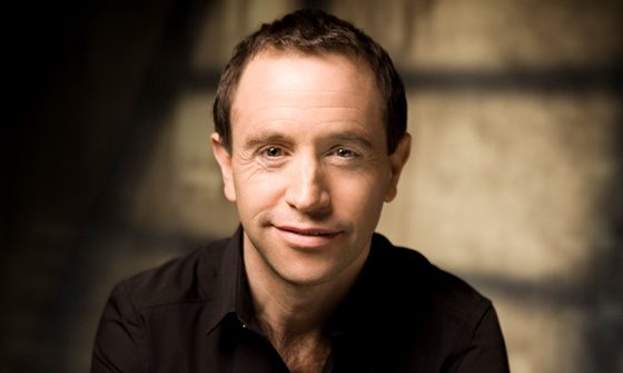 Mark Wigglesworth wearing a black shirt, smiling at the camera