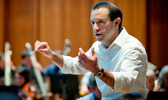 Mark Wigglesworth wearing a white shirt and holding a baton, conducting an orchestra
