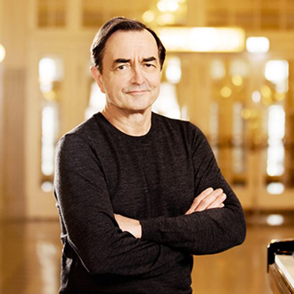 Pierre-Laurent Aimard sat next to a piano with his arms crossed