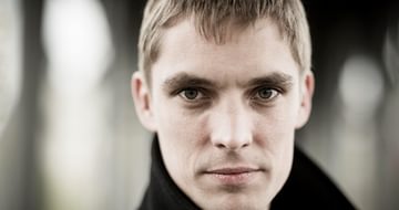 Cédric Tiberghien, a man with short hair and a black coat gazing directly at the camera, on a blurred, neutral background