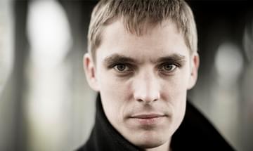 Cédric Tiberghien, a man with short hair and a black coat gazing directly at the camera, on a blurred, neutral background