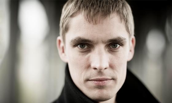 Cédric Tiberghien, a man with short hair and a black coat gazing directly at the camera, on a blurred, neutral background