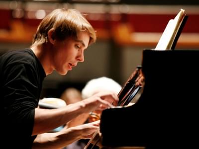 Cédric Tiberghien wearing a black shirt and playing a grand piano
