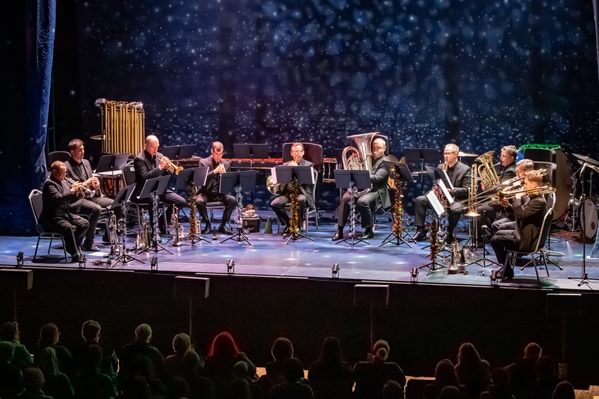 An ensemble of brass musicians (Philharmonia) performing on a dimly lit stage with starry backdrop