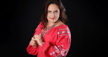 Maria Pukhlianko, a woman in a red embroidered blouse posing against a black background, looking softly towards the camera