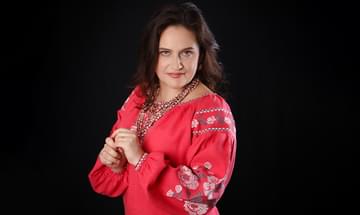 Maria Pukhlianko, a woman in a red embroidered blouse posing against a black background, looking softly towards the camera