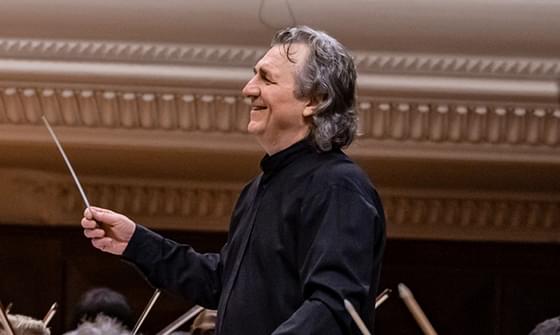 Volodymyr Sirenko in a black suit holding a baton, leading an orchestra and smiling