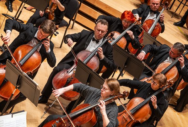 A birds eye picture of the cello section where seven people are playing all in black outfits