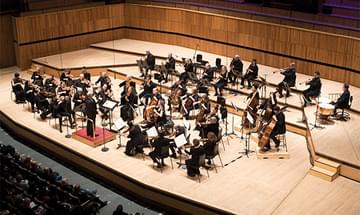 The Orchestra of the Age of Enlightenment performing on a wooden stage with musicians in formal attire, playing various instruments