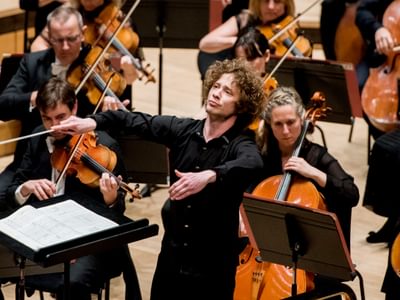 Santtu-Matias Rouvali, a conductor, passionately directing musicians on stage, including violinists and cellists