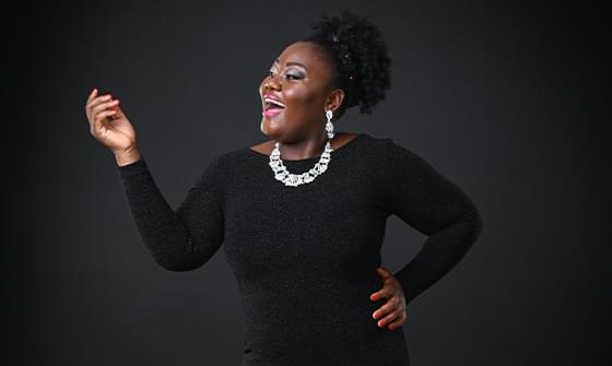 Masabane Cecilia Rangwanasha, a black woman in a black dress and sparkling jewellery, laughing against a dark background