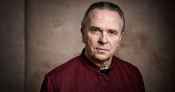 Sir Mark Elder headshot. He wears a red shirt and looks at the camera
