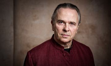 Sir Mark Elder headshot. He wears a red shirt and looks at the camera