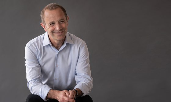 Mark Wigglesworth, an older balding white man in a white shirt smiling and looking off to the right