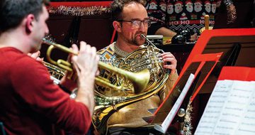 A group of men in Christmas jumpers surrounded by tinsel playing various brass instruments