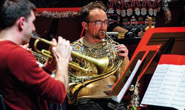 A group of men in Christmas jumpers surrounded by tinsel playing various brass instruments