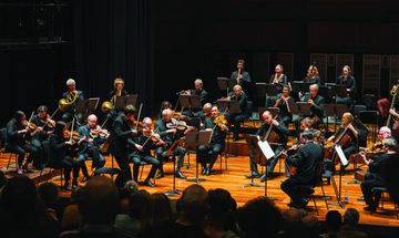 The Orchestra of the Age of Enlightenment performing on a dark stage, they're all wearing black