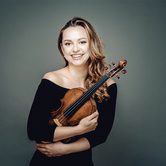 Maria Ioudenitch, a young white woman with long blonde hair in a black dress hugging a violin