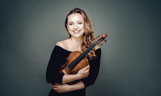Maria Ioudenitch, a young white woman with long blonde hair in a black dress hugging a violin