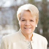 Marin Alsop, an older white woman with short light blonde hair in a snowy garden in a white blouse and jacket