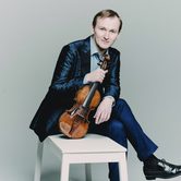 Nikita Boriso-Glebsky an older white man with light brown hair sat on a stool in a black suit holding a violin by the neck