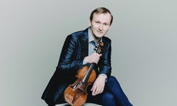 Nikita Boriso-Glebsky an older white man with light brown hair sat on a stool in a black suit holding a violin by the neck