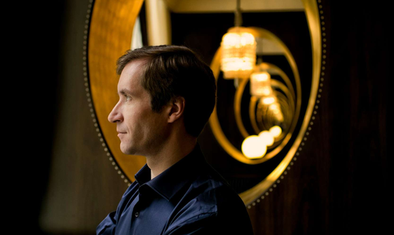 Nikolai Lugansky a white man with short brown hair in a dark blue shirt in front of a gold mirror. He's looking to the left with his arms crossed