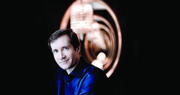 Nikolay Lugansky a white man with short brown hair in a blue shirt with circular lights behind him