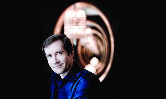 Nikolay Lugansky a white man with short brown hair in a blue shirt with circular lights behind him