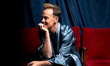 Jason Donovan sat on theatre chairs leaning on his hand