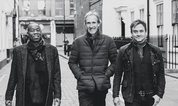 Three members of Mike + The Mechanics walking along a street and smiling at the camera
