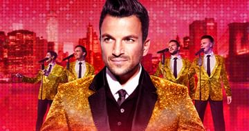 Peter Andre wearing a gold sparkly jacket stood in front of four other male singers wearing the same outfit, singing into microphones, on a red city skyline background
