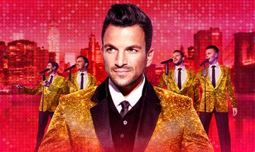 Peter Andre wearing a gold sparkly jacket stood in front of four other male singers wearing the same outfit, singing into microphones, on a red city skyline background