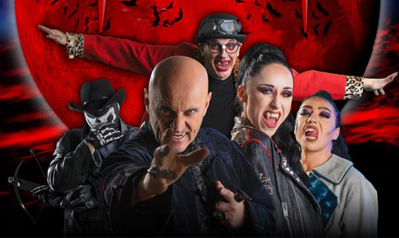 Five costumed individuals posing dramatically in front of a large red moon with bat silhouettes