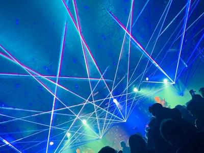 Concert scene with vibrant blue and green laser lights crisscrossing above a crowd